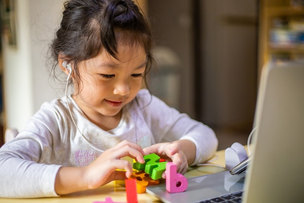 Asiatisches Mädchen lernt online Alphabete, glückliches Mädchen lernt online mit Laptop zu Hause.