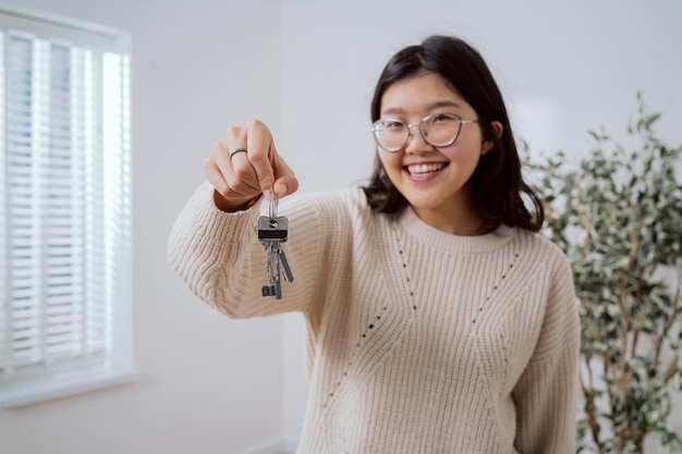 Asiatisches Mädchen mit Brille steht in neu gekaufter Wohnung in der Hand und hält die Schlüssel