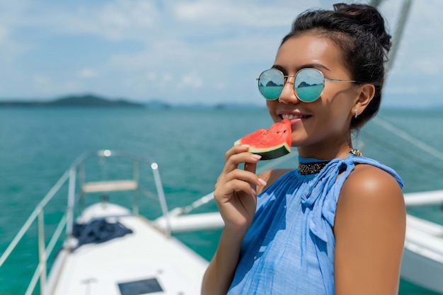 Asiatisches Mädchen mit Gläsern isst eine Wassermelone auf einer Yacht. Luxusreisen. Sommerferien.