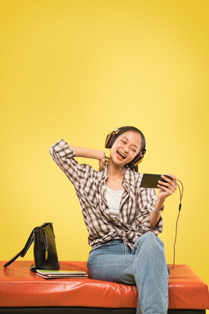 Asiatisches Mädchen mit Kopfhörern mit Smartphone beim Sitzen mit Büchern und Tasche