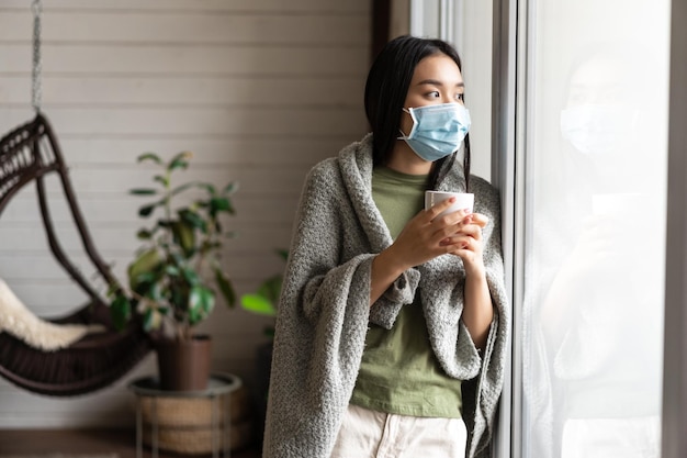 Asiatisches Mädchen mit Sehnsucht nach medizinischer Gesichtsmaske geht nach draußen, ist an Covid erkrankt und bleibt auf Selbstquara ...