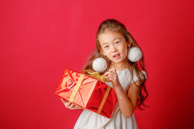 Asiatisches Mädchen mit Weihnachtsbaumspielzeug auf rotem Hintergrund, Weihnachten