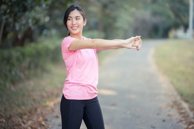 Asiatisches Mädchen streckt ihre warmen Körpermuskeln, bevor es zum Laufen im Park ausgeht