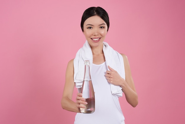 Asiatisches Mädchen wirft mit dem Wasser auf, das auf rosa Hintergrund lokalisiert wird.