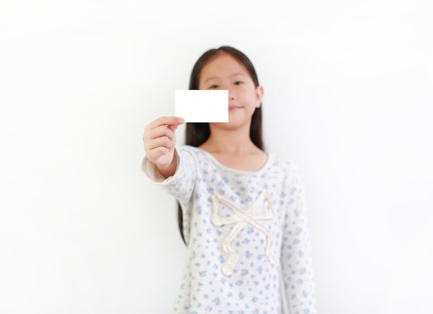 Asiatisches Mädchenkind, das leere weiße Karte über weißem Hintergrund zeigt Konzentrieren Sie sich auf die Karte in der Hand des Kindes