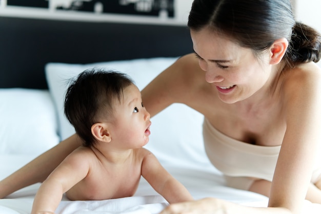 Asiatisches nettes Baby, das mit ihrer schönen Mutter auf dem Bett kriecht und spielt.