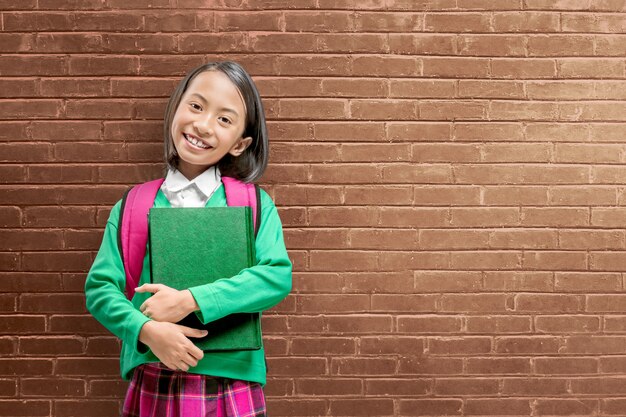Asiatisches nettes Mädchen mit einem Rucksack, der die Buchstellung hält