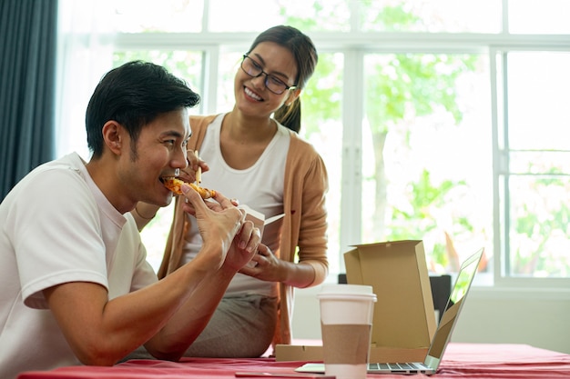 Asiatisches Paar, das zusammen Instant-Nudeln und Pizza in der Küche isst. Genießen Sie eine gesunde Mahlzeit. Lebensstil zum Abendessen und bleiben Sie zu Hause. Frau isst Instant-Nudeln.