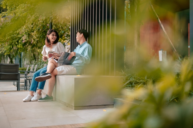 Asiatisches Paar liest Buch im Park am Hotel. Urlaub, Liebespaar und süßes Paarkonzept.