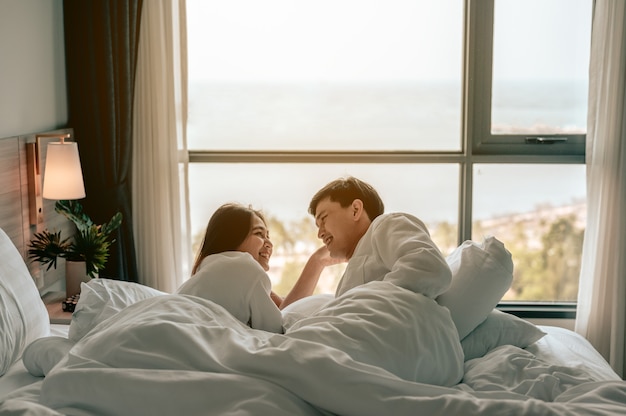Asiatisches Paar umarmt und lächelt auf dem Bett in einem Schlafzimmerabend sitzenPaar am Valentinstag