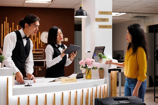 Asiatisches Personal nimmt an der Rezeption eine Reservierung für den Kunden vor. Lächelnder Concierge beim Einchecken eines Kunden. Touristin erhält Ratschläge vom freundlichen Personal. Tourist wird im eleganten Hotel begrüßt.