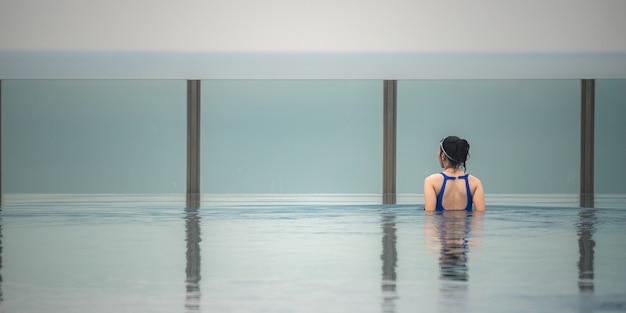 Asiatisches Reisekonzept. junge Frau, die den Blick auf den Stadthimmel vom Pool auf dem Dach des Hotels genießt, schöner Mädchenlebensstil im Freien in der Urlaubszeit