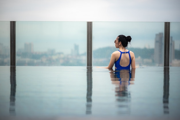 Asiatisches Reisekonzept. junge Frau, die den Blick auf den Stadthimmel vom Pool auf dem Dach des Hotels genießt, schöner Mädchenlebensstil im Freien in der Urlaubszeit