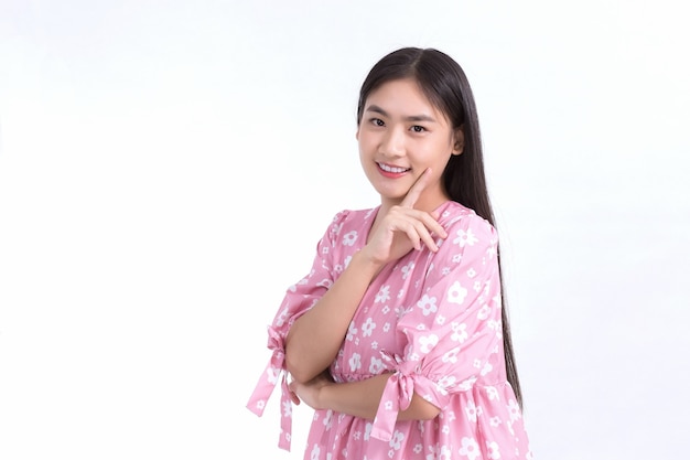 Asiatisches schönes Mädchen im rosa Kleid und im schwarzen langen Haar. Ihre Hände berühren Wangenlächeln, zeigen schöne Haut auf weißem Hintergrund.