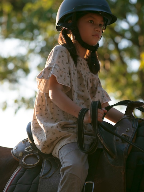Asiatisches Schulkind mit Pferd, das reitet oder das Pferdereiten auf Pferderanch übt.