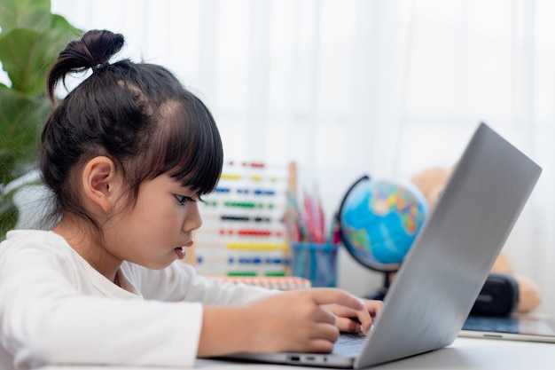 Asiatisches Schulmädchen, das zu Hause ihre Hausaufgaben mit Laptop macht Kinder verwenden Gadgets, um zu lernen Bildung und Fernunterricht für Kinder Homeschooling während der Quarantäne Bleiben Sie zu Hause