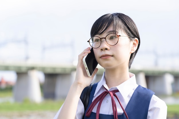 Asiatisches Schulmädchen mit schwarzen kurzen Haaren, die auf einem Smartphone sprechen