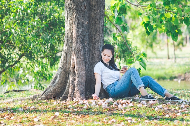 Asiatisches Sitzen der jungen Frau, das unter einem Baum sich entspannt