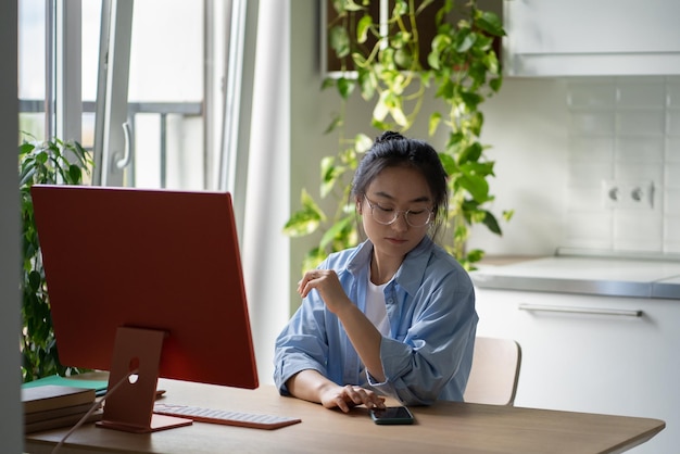 Asiatisches Studentenmädchen, das während des Online-Studiums das Telefon überprüft Digitale Ablenkungen im E-Learning