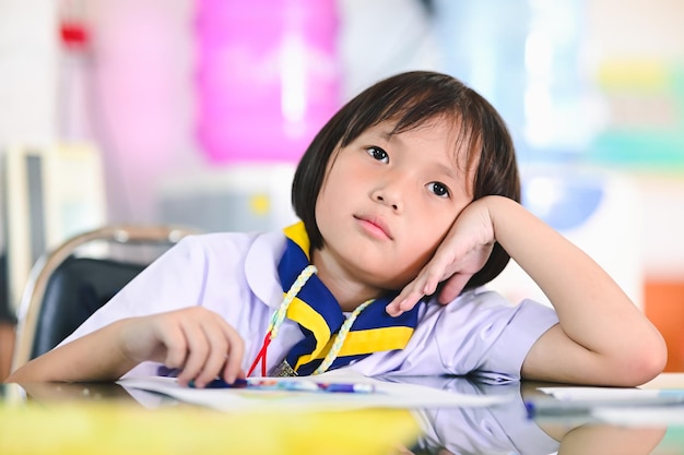 Asiatisches Studentenmädchen trauriges oder gelangweiltes kleines Studentenmädchen in einheitlicher Kinderlernprüfung im Klassenzimmer löste Beispiele, die Übungen im Schularbeitsbuch machten