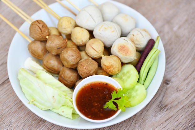 Asiatisches thailändisches Essen gegrillte Fleischbällchen Fischbällchen und Schweinefleischbällchen mit würziger Sauce, Fleischbällchen auf Spießen auf weißem Teller und frischem Gemüse Kohlgarten lange Bohnengurke