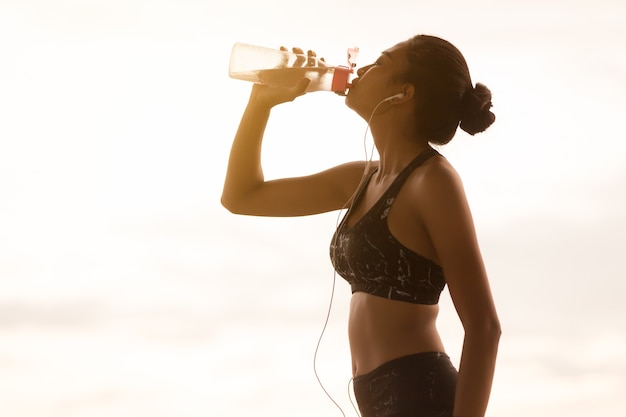 Asiatisches Trinkwasser der jungen Frau, nachdem Sonnensatz gerüttelt worden ist