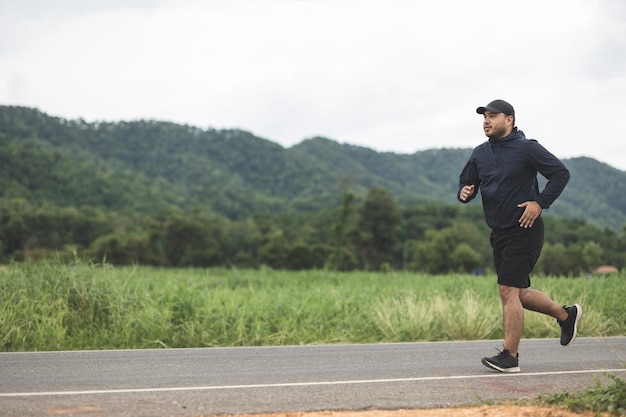 Asien-Mann, der Sportkleidung trägt, die auf der Straße mit Berghintergrund läuft. Junger Mann joggt für Bewegung in der Natur. gesundes lebensstil- und sportkonzept