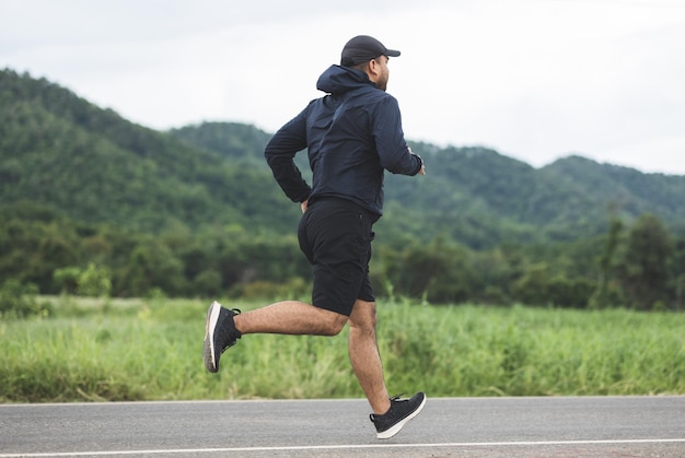 Asien-Mann, der Sportkleidung trägt, die auf der Straße mit Berghintergrund läuft. Junger Mann joggt für Bewegung in der Natur. gesundes lebensstil- und sportkonzept