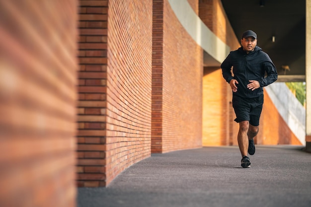 Asien Mann trägt Jacke Sportbekleidung läuft auf der Straße unter dem Gebäude Junger Mann joggt für Bewegung in der Stadt gesunder Lebensstil und Sportkonzept