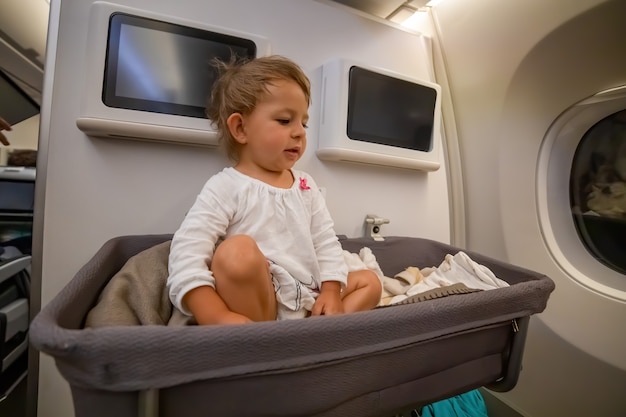 Asiento de bebé niña en una cuna especial en el avión bebé mira al costado en el moisés en avión