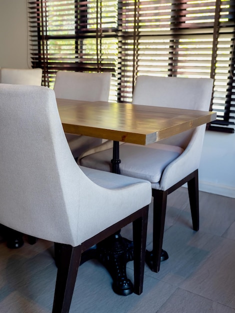 Asiento de silla de tela gris moderno vacío y mesa de comedor de madera estilo vintage cerca de la ventana decorada con estilo vertical de persiana negra Diseño de interiores de comedor en el interior del hotel