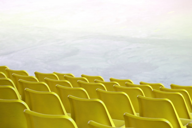 Los asientos amarillos plásticos vacíos reman en la demostración interior del estadio o el fondo del lugar del campo de deporte.