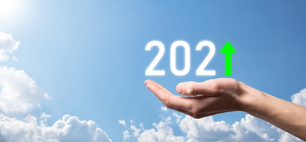 Asimiento de la mano 2021 icono positivo en el fondo del cielo. Planifique el crecimiento positivo del negocio en el concepto del año 2021. Plan de empresario y aumento de indicadores positivos en su negocio, conceptos de negocio creciendo.