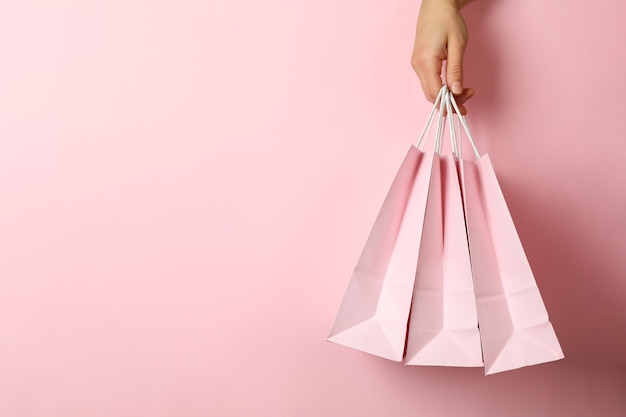 Asimiento de la mano femenina bolsas de la tienda sobre fondo rosa