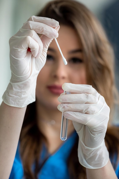 Asimiento de la mano femenina con hisopo de esputo respiratorio en tubo de ensayo para diagnóstico de COVID-19. cuidado de la salud