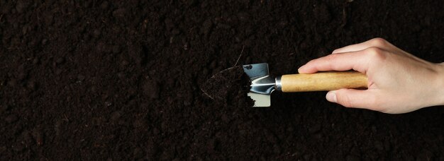 Asimiento de la mano femenina pala para jardinería en el fondo del suelo