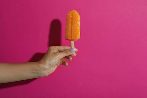 Asimiento de la mano femenina palo de helado en rosa