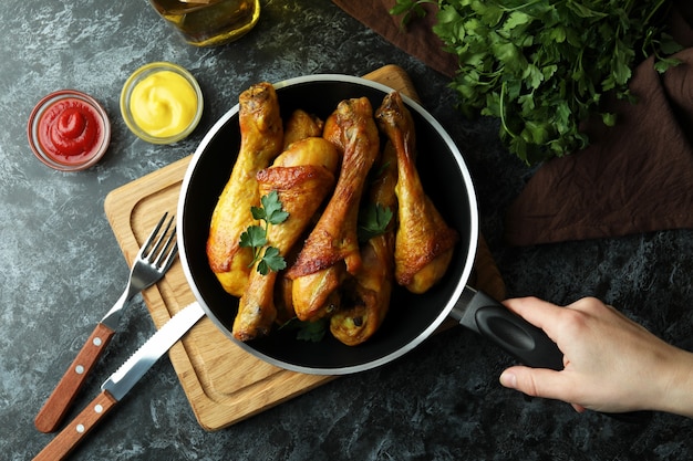 Asimiento de la mano femenina sartén con muslos de pollo asado