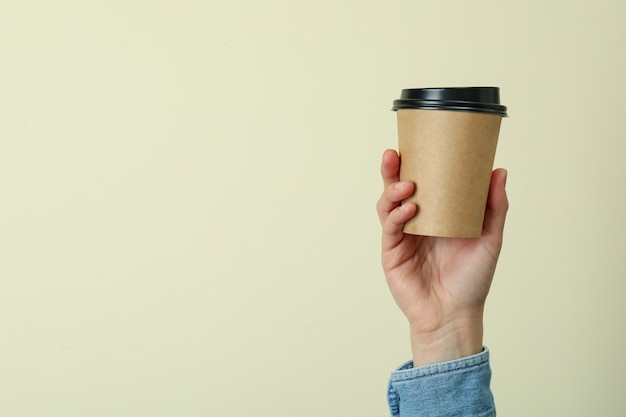 Asimiento de la mano femenina taza de papel sobre superficie beige