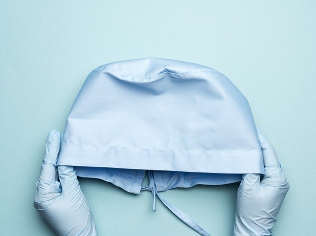 Asimiento de la mano gorra médica textil azul con lazos para médico, cirujano sobre fondo azul, vista superior
