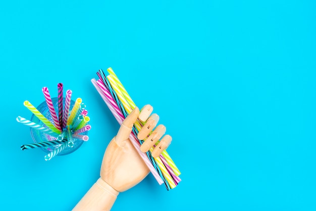 Asimiento de la mano de madera pajitas con rayas para fiesta en vidrio sobre fondo azul.