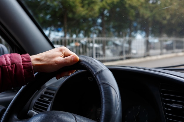 Asimiento de la mano masculina volante en cuero negro, hombre conduciendo, concepto de transporte,