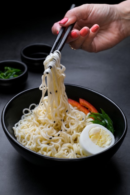 Asimiento de la mano palillos de fideos con vapor sobre fondo negro concepto de comida chatarra de fideos asiáticos