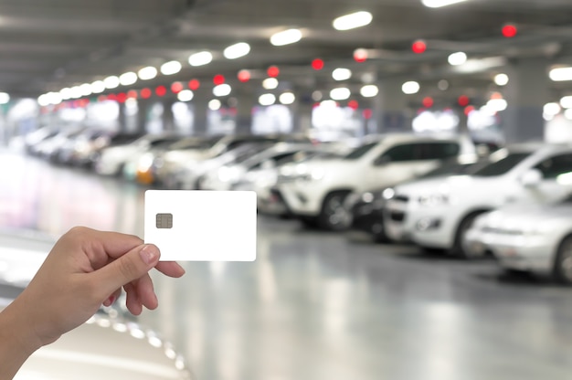 asimiento de la mano tarjeta en blanco en el estacionamiento del coche borroso con luz bokeh Fondo