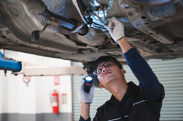 Asimiento mecánico masculino asiático y linterna brillante para examinar el automóvil debajo del chasis