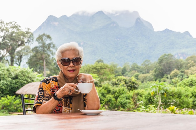 Asin graue weiße Haare Seniorin trinkt Kaffee im Café im Freien mit Blick auf die Berge