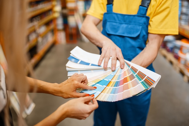 Asistente y clienta con paleta de colores en ferretería. Vendedor en uniforme y mujer en tienda de bricolaje, compras en el supermercado del edificio