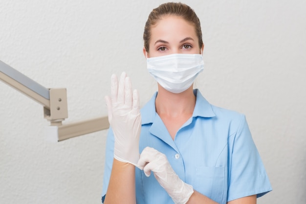 Asistente dental en la máscara mirando la cámara tirando de los guantes