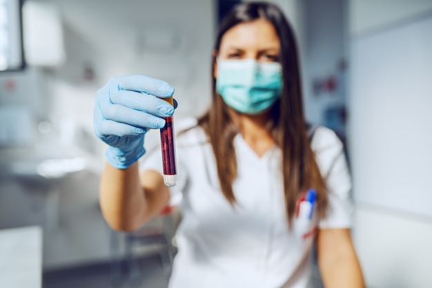 Asistente de laboratorio caucásico hermoso que sostiene el tubo de ensayo con sangre mientras está parado en el laboratorio.