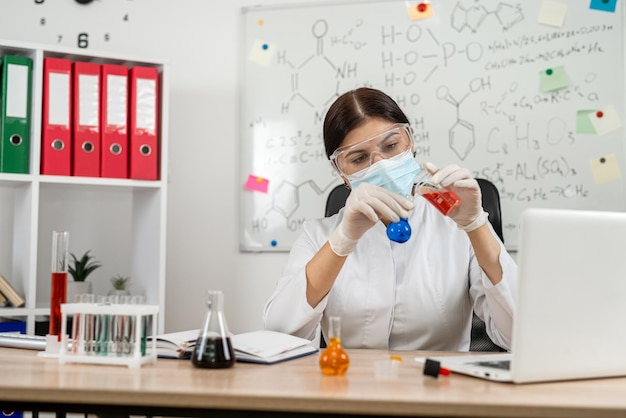 Asistente de laboratorio caucásico mujer vertiendo muestra en un matraz en el laboratorio